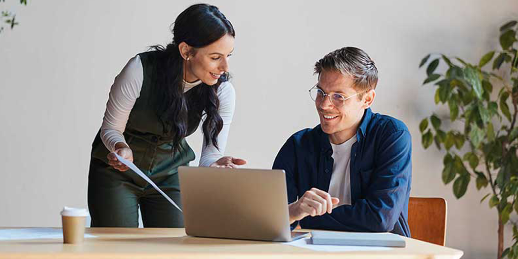 man and woman having a pleasant discussion sitting at a table in front of a laptop